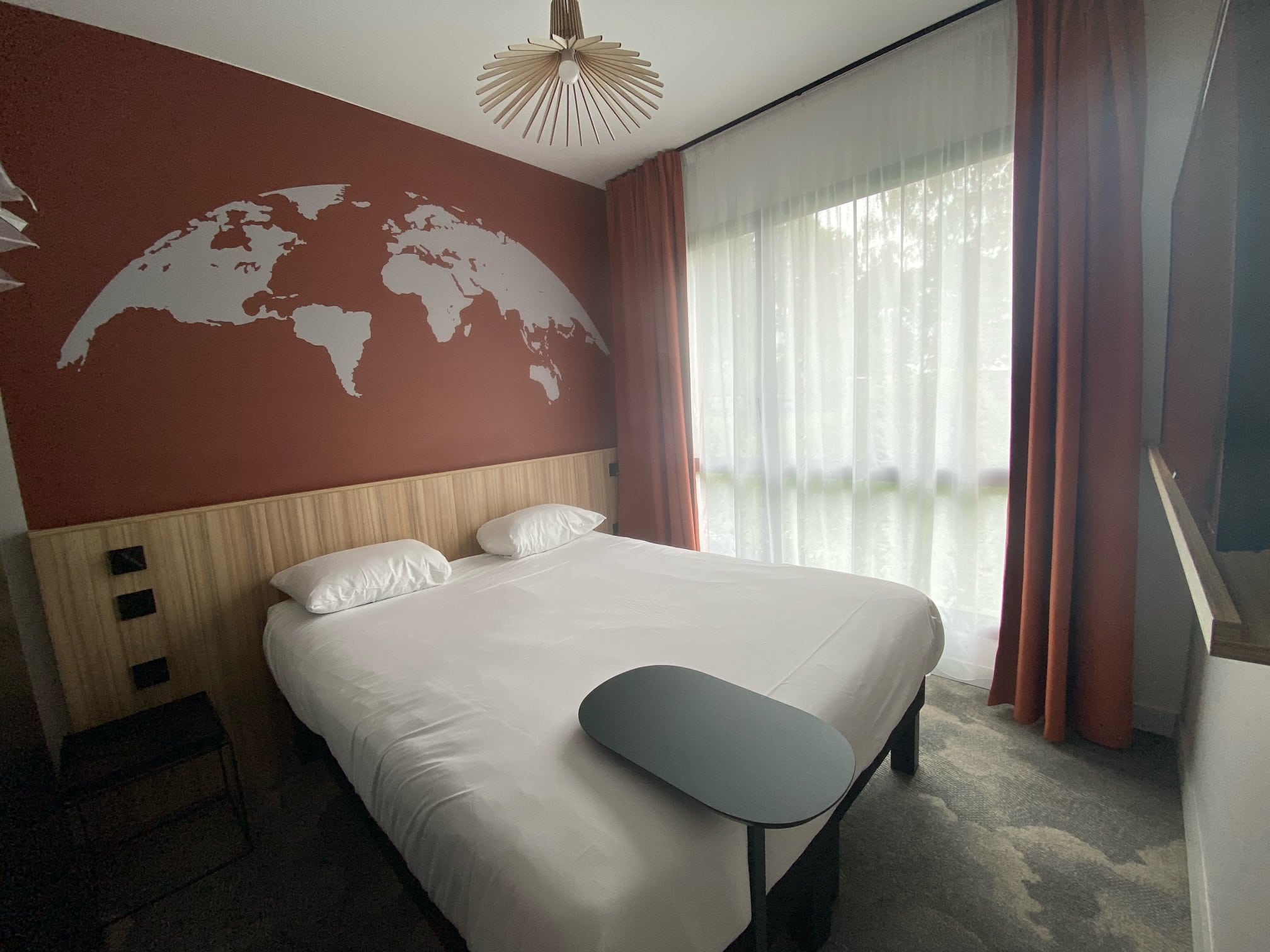 Chambre d’hôtel avec rideaux occultants M1 en polyester FR et voilage léger non feu installés sur baie vitrée