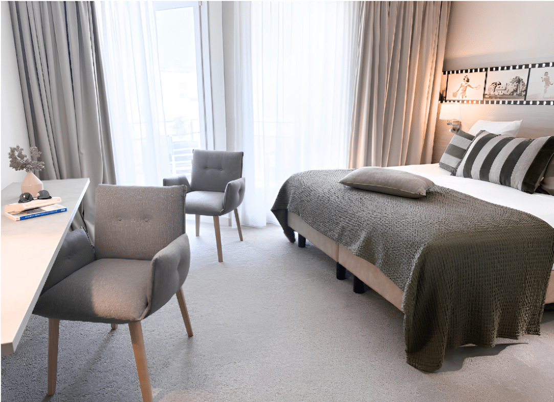 Chambre d’hôtel avec chemin de lit olive, coussins décoratifs verts, rideaux beiges et voilages blancs.