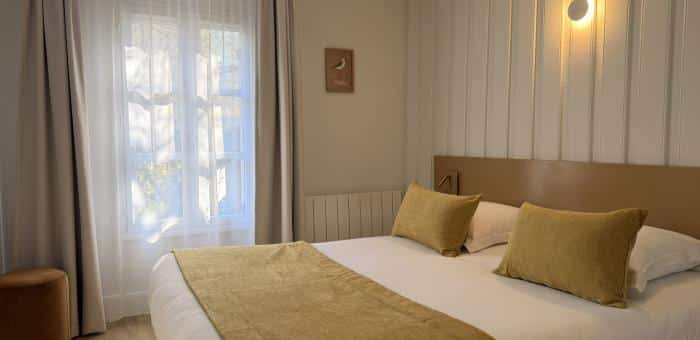 Chambre privilège avec lit double, coussins dorés, voilage blanc lumineux, applique sphérique et tableau oiseau au Cap Hornu