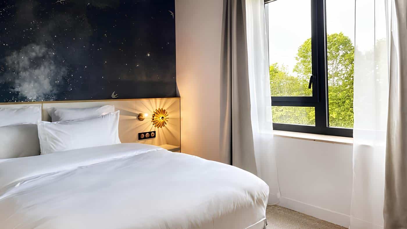 Suite Junior de l’OSMO Hôtel avec fenêtre habillée d’un voilage blanc et de rideaux beiges