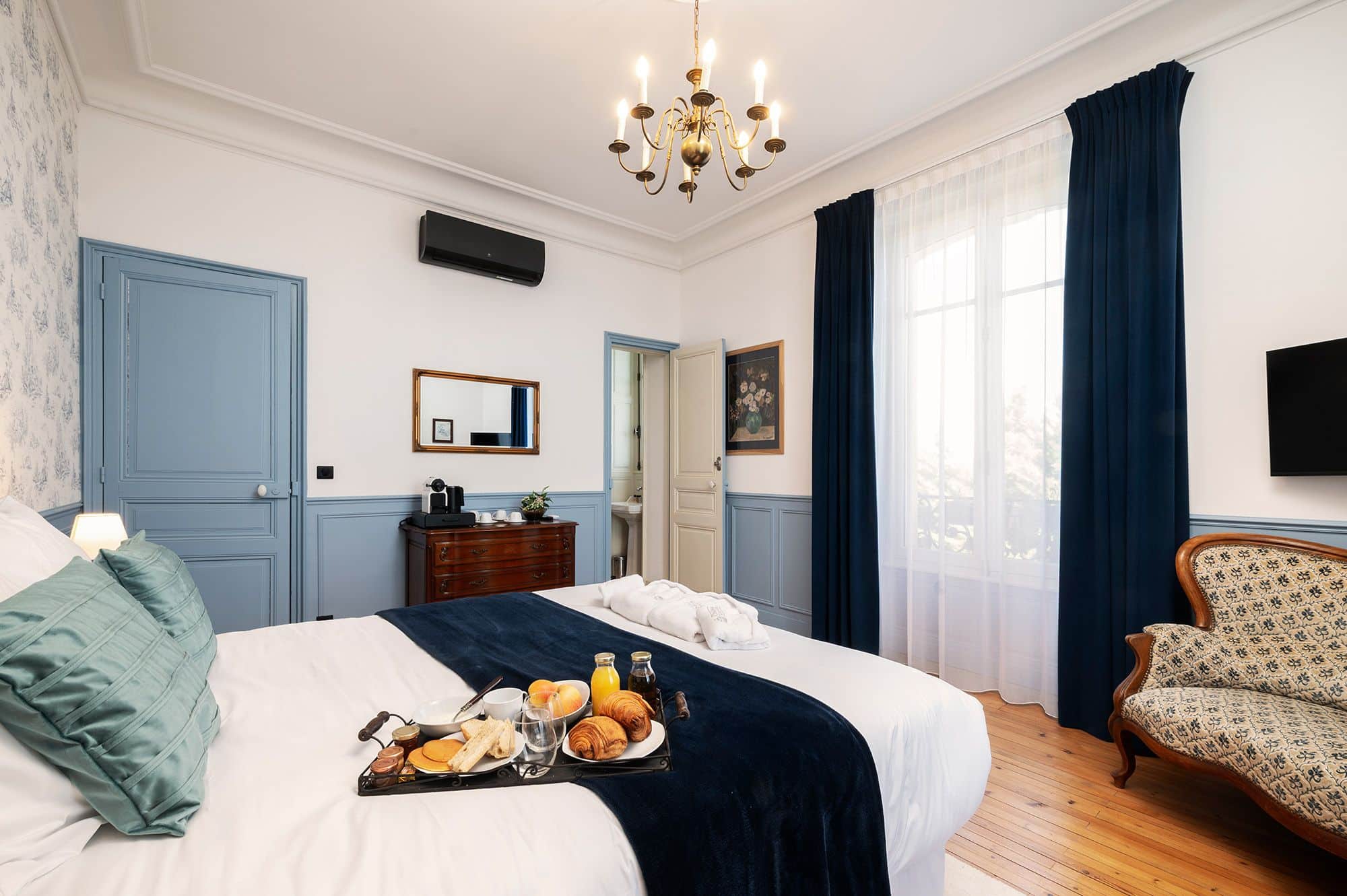 Rideaux bleu marine et voilage blanc encadrant une fenêtre dans une chambre avec lit blanc et chemin de lit bleu.